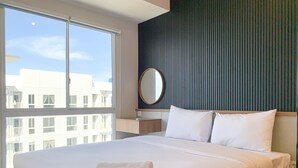 A hotel room with a large bed, a bedside table, a round mirror, and a view of the city through a large window. - Stylisth 1Br At Tokyo Riverside Pik 2 Apartment (Teluknaga)