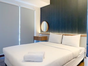 A modern hotel room with a large bed, a wooden nightstand, a round mirror, and a dark textured wall. - Stylisth 1Br At Tokyo Riverside Pik 2 Apartment (Teluknaga)