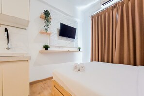 Quarto de hotel com uma cama, televisão na parede, uma planta pequena e uma janela com cortinas.
