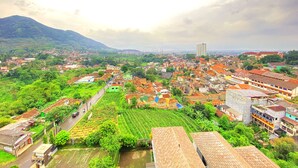 A panoramic view of a city with a mix of residential and commercial buildings, surrounded by lush greenery and hills in the background. - Good Deal Studio Room At Taman Melati Jatinangor Apartment (Hegarmanah)