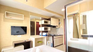 A hotel room with a bed, a TV, a kitchenette, and a bathroom. - Good Deal Studio Room At Taman Melati Jatinangor Apartment (Hegarmanah)
