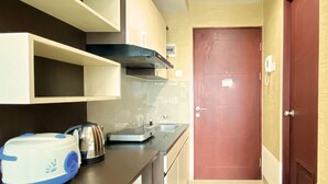 A compact kitchen with a microwave, kettle, and a small countertop. There is a door with a lock and a phone on the wall. - Good Deal Studio Room At Taman Melati Jatinangor Apartment (Hegarmanah)