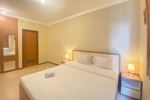 A hotel room with a large bed, two bedside tables with lamps, a wooden door, and a mirror.