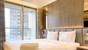 A hotel room with a large bed, a nightstand, a wooden headboard, a window with curtains, and a view of buildings outside.