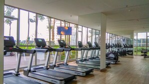 A gym with multiple treadmills aligned in rows, large windows, and a flat-screen TV mounted on the wall.