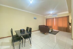 Uma sala de jantar com mesa e cadeiras, um sofá e uma janela com cortinas.