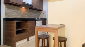A modern kitchen with dark wooden cabinets, a black countertop, and a small dining table with stools. - Warm And Homey 1Br At Belmont Residence Puri Apartment (Jakarta)