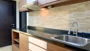 A modern kitchen with a black countertop, stainless steel sink, wooden cabinets, and a tiled backsplash. - Warm And Homey 1Br At Belmont Residence Puri Apartment (Jakarta)