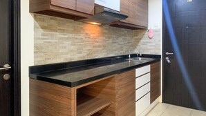 A modern kitchen with wooden cabinets, a black countertop, and a tiled backsplash. - Warm And Homey 1Br At Belmont Residence Puri Apartment (Jakarta)
