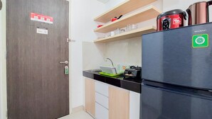 A compact kitchen with a dark wooden door, a stainless steel refrigerator, and a microwave on the countertop. - Enjoy Living And Warm Studio At Serpong Garden Apartment (Cisauk)