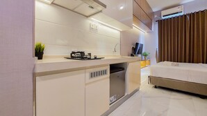 A modern kitchen with a built-in stove, a microwave, and a sink. There is a small plant on the counter and a TV mounted on the wall. - Scenic Designed And Comfy Studio At Sky House Bsd Apartment (Pagedangan)