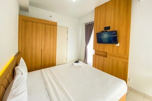 A hotel room with a bed, wooden wardrobe, a television mounted on the wall, and a window with curtains. - Comfort 1Br At Patraland Urbano Apartment (Bekasi)