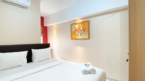 A hotel room with a bed, white linens, a painting on the wall, and a towel rack with towels. - Good Deal And Well Furnished 2Br At Springlake Summarecon Bekasi Apartment (Bekasi)