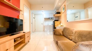 A modern living room with a flat-screen TV, wooden entertainment unit, beige sofa, and a kitchen in the background. - Good Deal And Well Furnished 2Br At Springlake Summarecon Bekasi Apartment (Bekasi)