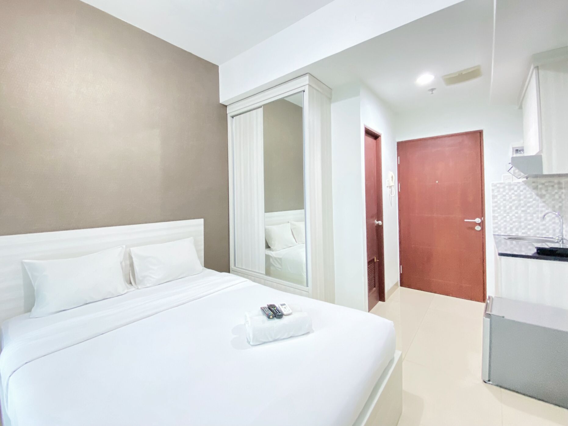A hotel room with a large bed, a wardrobe, and a kitchenette.