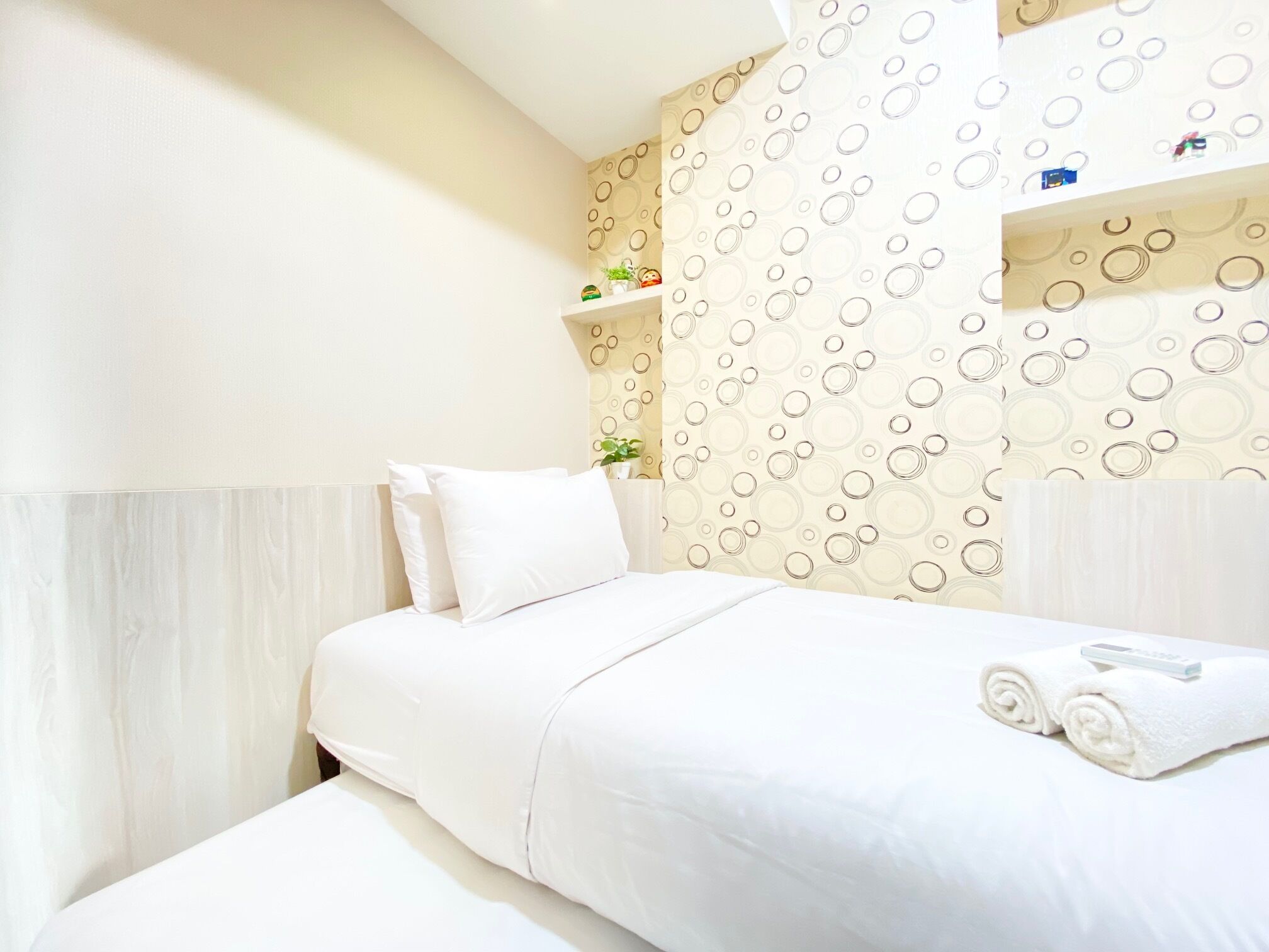 A neatly made bed with white linens, a small bedside table with a lamp, and a wall with a circular pattern.