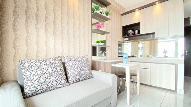 A modern living room with a sofa and a small table, a kitchen area with cabinets and a countertop, and a decorative wall with a textured pattern. - Chic And Cozy 2Br At Mekarwangi Square Cibaduyut Apartment (Bandung)