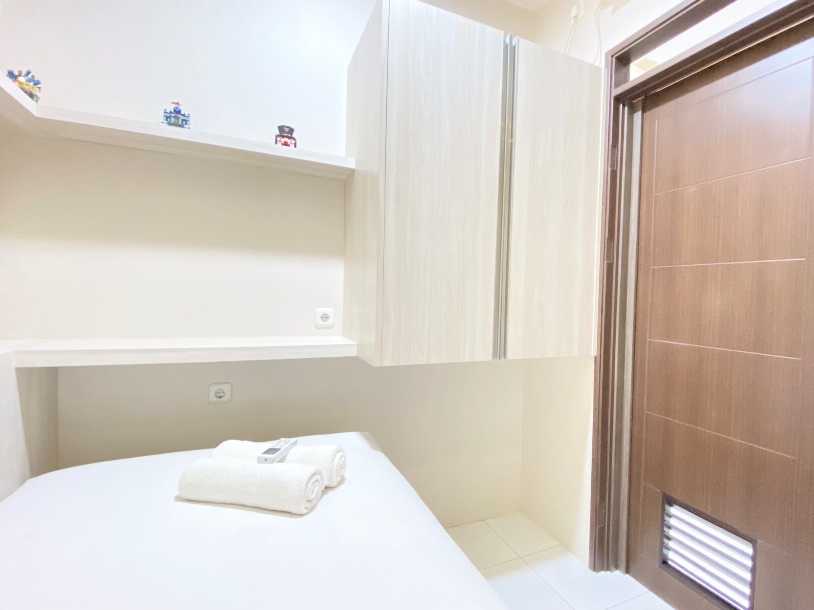 A hotel room with a bed, a wooden door, and a small shelf with decorative items.