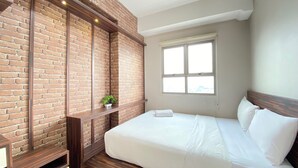 A bedroom with a brick wall, a window, a bed, and a small plant. - Chic And Cozy 2Br At Mekarwangi Square Cibaduyut Apartment (Bandung)