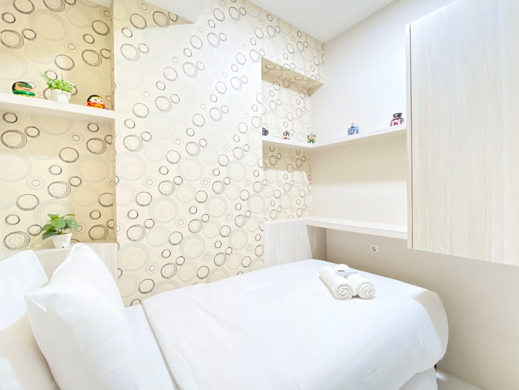 A hotel room with a bed, a shelf with decorative items, and a wall with a circular pattern.