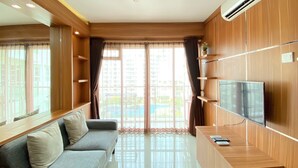 Ein modernes Wohnzimmer mit grauem Sofa, einer Holz-Unterhaltungseinheit mit Fernseher und großen Fenstern mit Vorhängen.