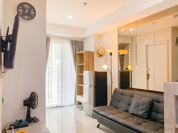 A modern living room with a grey sofa, a large mirror, and a clock on the wall. - Comfort And Enjoy Living 2Br At Daan Mogot City Apartment (Jakarta)