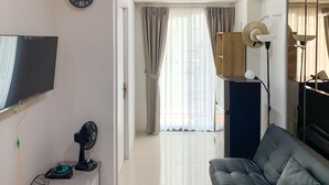 A modern living room with a flat-screen TV, a black sofa, a standing fan, and a wooden cabinet. - Comfort And Enjoy Living 2Br At Daan Mogot City Apartment (Jakarta)