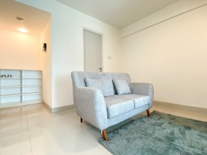 A living room with a grey sofa, a white shelving unit, and a blue rug.
