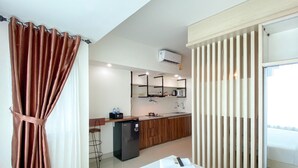 Una habitación de hotel moderna con cama, una kitchenette pequeña, un refrigerador y una ventana con persianas.