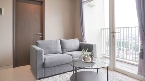 Una sala de estar moderna con un sofá gris, una mesa de centro de vidrio y vistas de la ciudad a través de amplios ventanales.