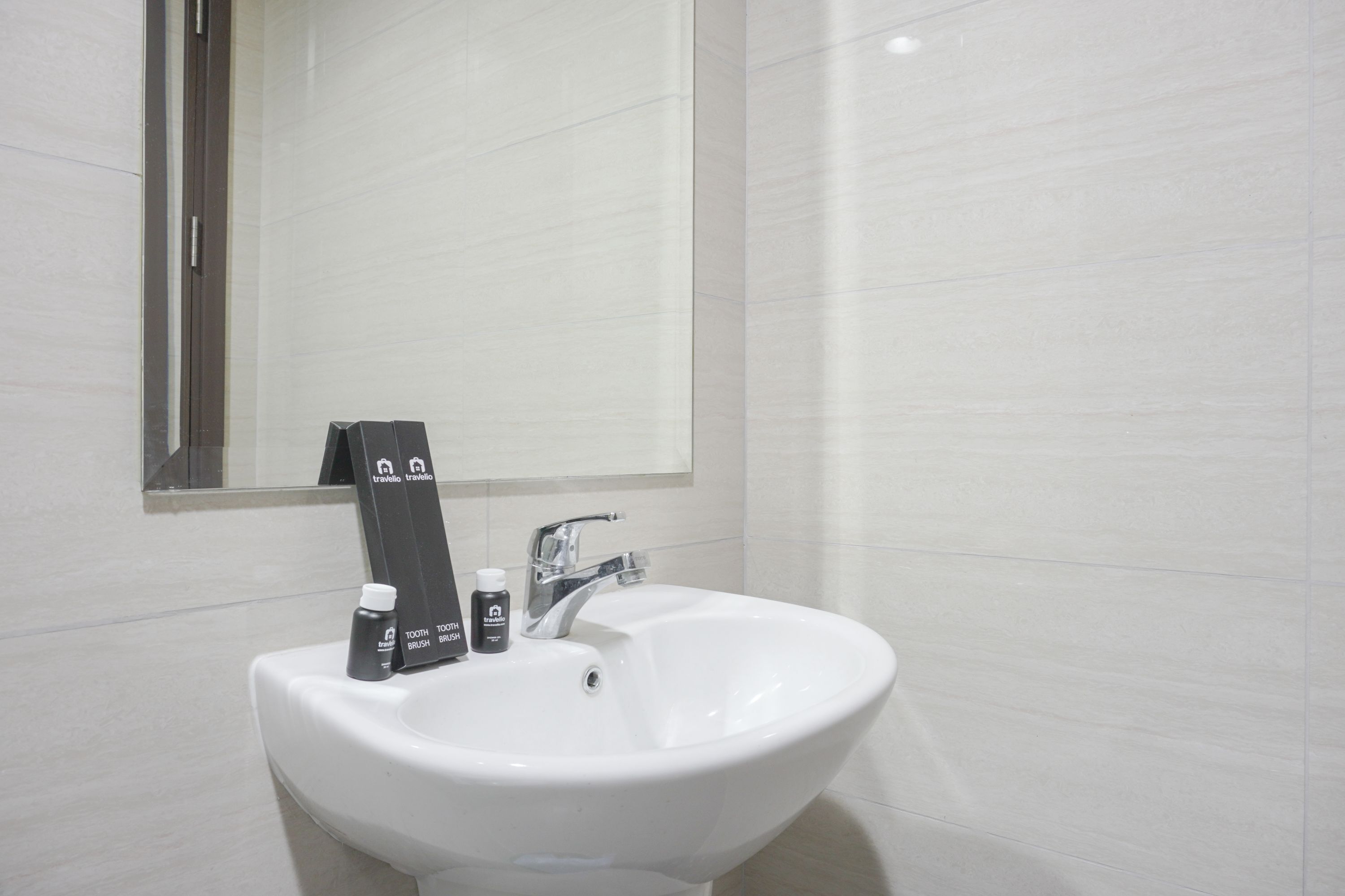 A white bathroom sink with a mirror above it, a toothbrush holder, and two bottles of mouthwash.