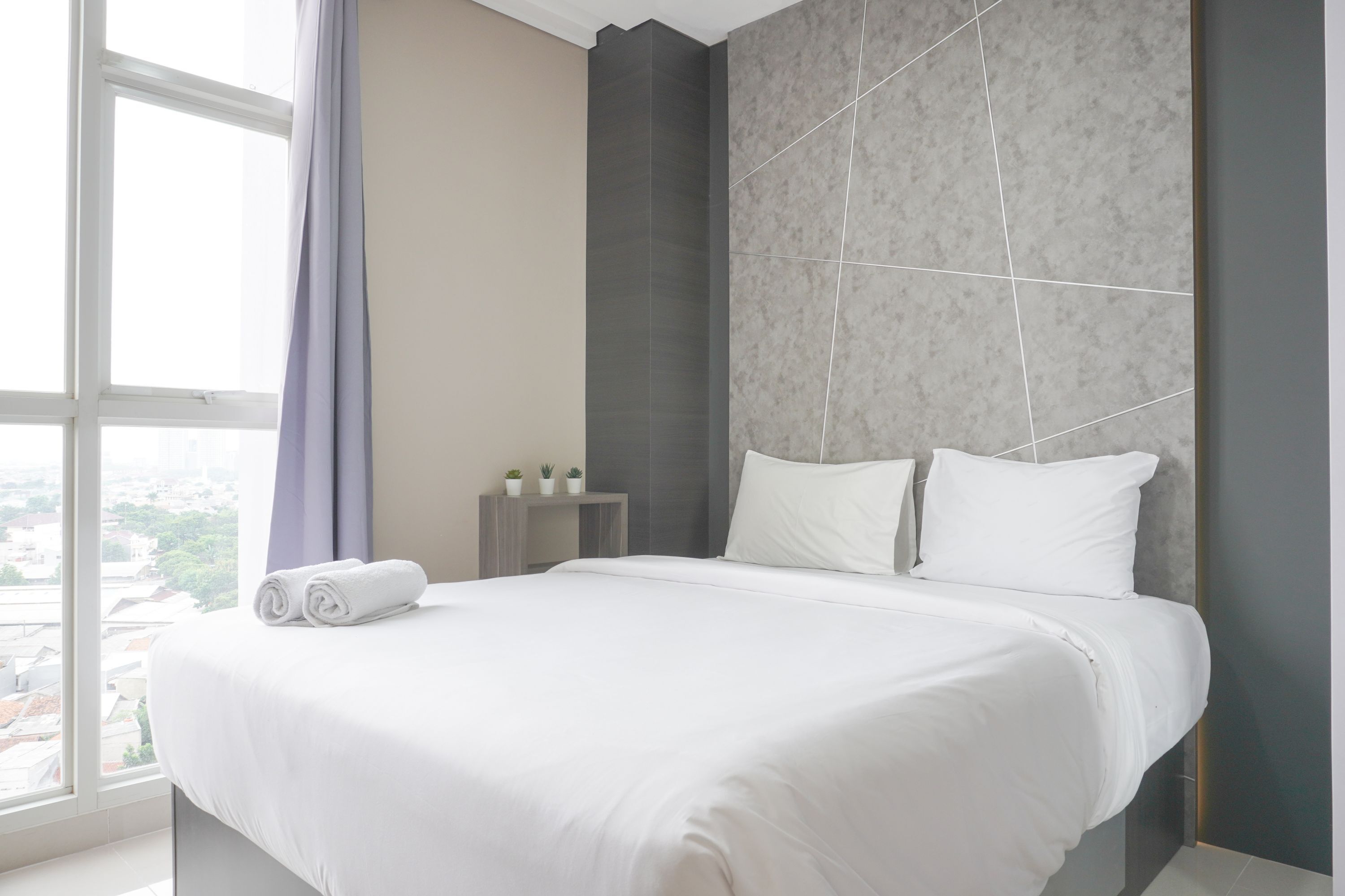 Une chambre d’hôtel moderne avec un grand lit, une vue par la fenêtre et une petite table de chevet agrémentée d’une plante.