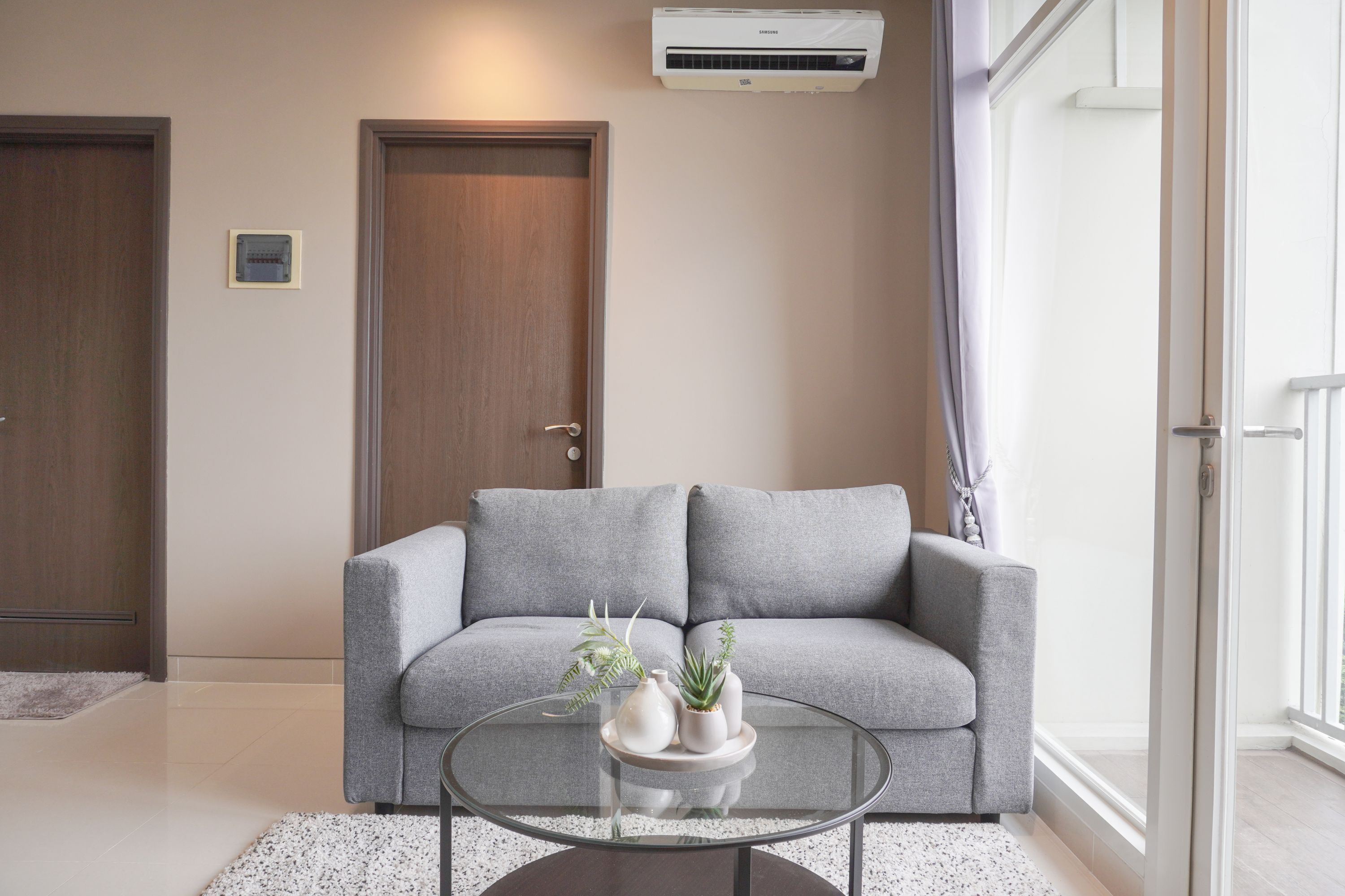 A living room with a grey sofa, a glass coffee table, and a small plant arrangement.