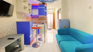 A modern living room with a blue sofa, a TV mounted on the wall, and a ceiling with a cloud pattern. - Graceful 2Br Apartment At Gateway Ahmad Yani Cicadas (Bandung)