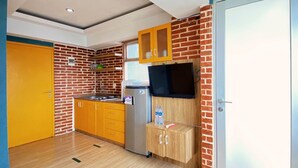 A compact kitchen with yellow cabinets, a refrigerator, and a wooden cabinet with a television. - Spacious And Unique 1Br At Jarrdin Cihampelas Apartment (Bandung)