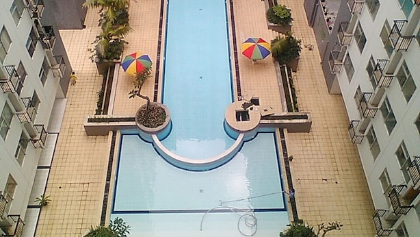 A swimming pool surrounded by a tiled walkway, with multiple umbrellas and potted plants. - Spacious And Unique 1Br At Jarrdin Cihampelas Apartment (Bandung)