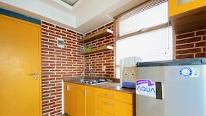 A compact kitchen with yellow cabinets, a brick accent wall, a stainless steel refrigerator, and a window with blinds. - Spacious And Unique 1Br At Jarrdin Cihampelas Apartment (Bandung)