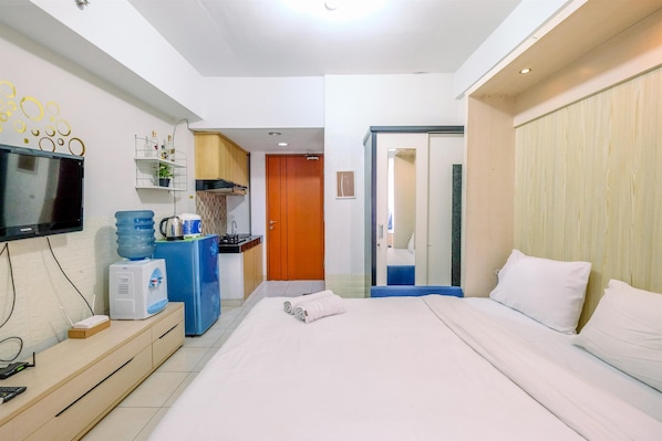 Une chambre d’hôtel équipée d’un lit, d’une télévision, d’un bureau avec un ordinateur, d’un distributeur d’eau et d’une armoire en bois.