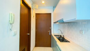 A compact kitchen with a stove, sink, and a wooden door. - Nice And Strategic Studio Apartment At Capitol Park Residence (Jakarta)