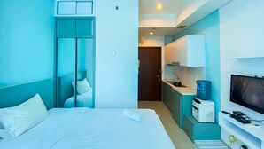 A hotel room with a bed, a TV, a mini-fridge, and a kitchenette. - Nice And Strategic Studio Apartment At Capitol Park Residence (Jakarta)