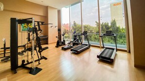 A gym with various exercise equipment, large windows, and a view of a cityscape. - Great Choice And Elegant 2Br At Capitol Suites Apartment (Jakarta)