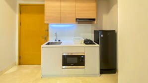 A compact kitchen with wooden cabinets, a built-in microwave, a gas stove, and a black refrigerator. - Great Choice And Elegant 2Br At Capitol Suites Apartment (Jakarta)
