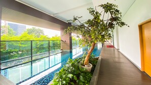 An indoor swimming pool with a wooden floor, surrounded by lush greenery and a glass barrier. - Great Choice And Elegant 2Br At Capitol Suites Apartment (Jakarta)