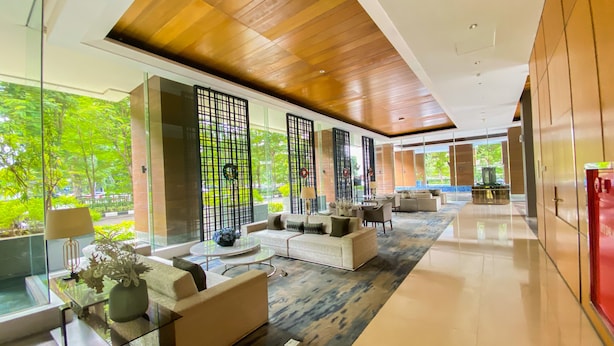 A modern hotel lobby with a glass partition, comfortable seating, and a view of greenery outside. - Great Choice And Elegant 2Br At Capitol Suites Apartment (Jakarta)