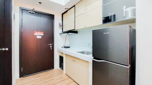 A compact kitchen with a dark door, a white countertop, a sink, and a black refrigerator. - Simply And Modern Studio At Casa De Parco Apartment (Pagedangan)