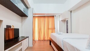 A modern bedroom with a bed, a TV, and a wooden floor. - Simply And Modern Studio At Casa De Parco Apartment (Pagedangan)