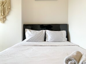 A neatly made bed with white linens and pillows, a black headboard, and a rolled towel on the side. - Studio With Minimalist Design Tokyo Riverside Pik 2 Apartment (Teluknaga)
