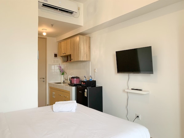 Une chambre d’hôtel équipée d’un lit, d’un téléviseur fixé au mur, d’une kitchenette avec une cuisinière et un évier, et d’un appareil de climatisation.