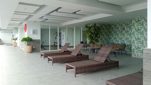 A spacious indoor area with wicker lounge chairs, a fitness area, and a wall with a tropical leaf pattern.