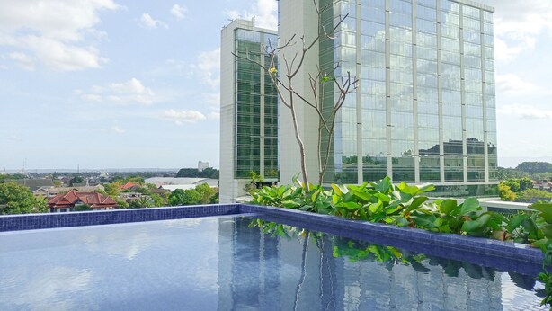 A modern building with a glass facade, a swimming pool with blue tiles, and surrounding greenery.